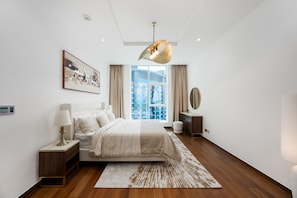 A modern bedroom with a large bed, a side table, a bedside lamp, a floor lamp, a large window, and a view of the city. - Refined 1BR Haven | Palm Jumeirah (Dubai)