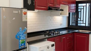 A compact kitchen with a refrigerator, washing machine, and red cabinets.