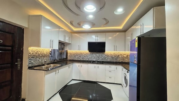 A modern kitchen with white cabinets, a black countertop, a built-in washing machine, and recessed ceiling lights.