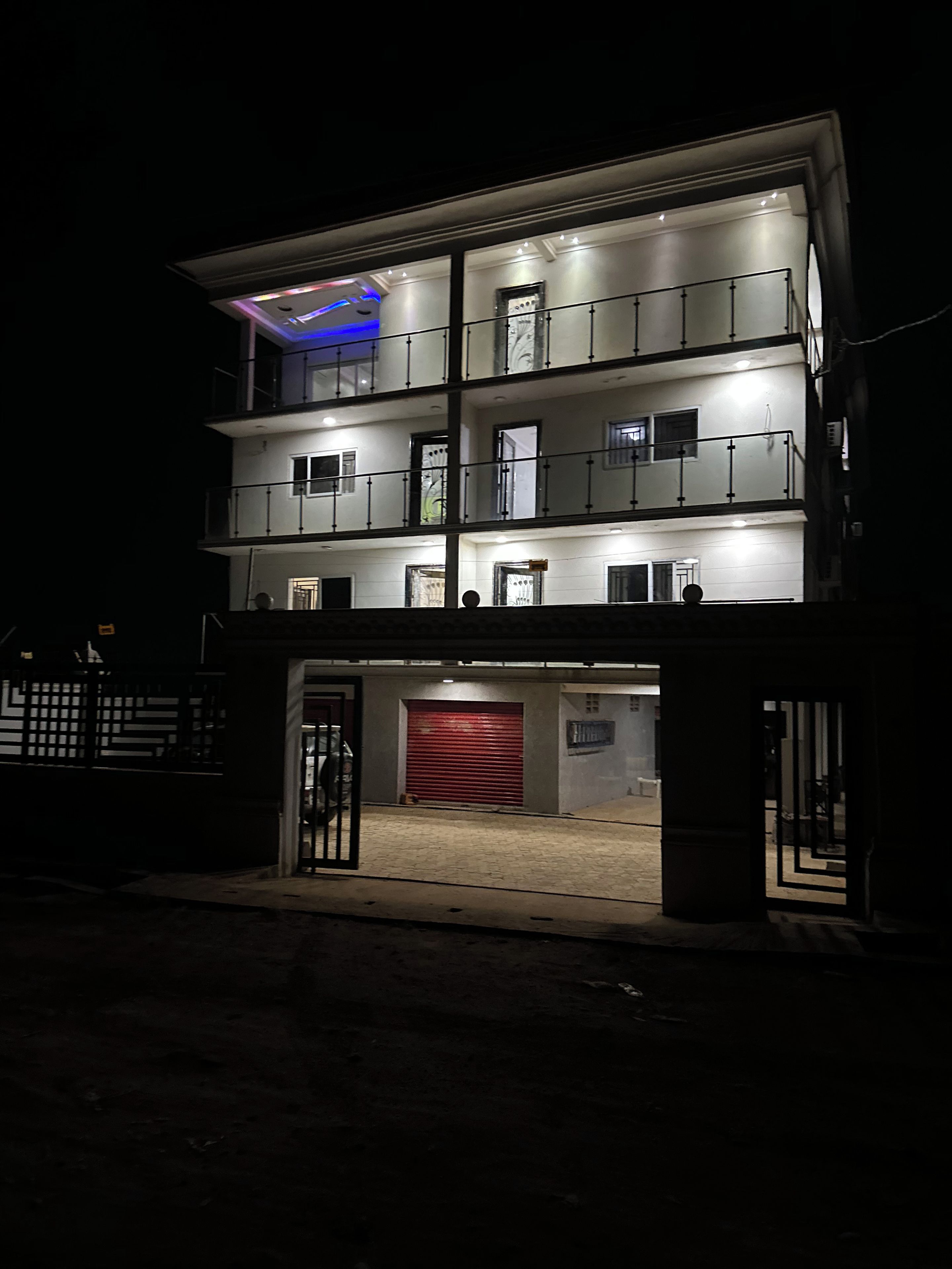 Un edificio de varios pisos con acceso a un garaje, balcones y un piso superior iluminado.