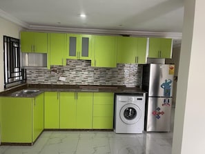 Una cocina con armarios verdes, lavadora y refrigerador.