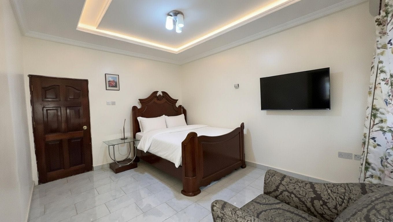 A bedroom with a bed, a television mounted on the wall, a sofa, and a door.