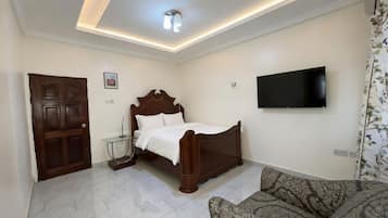 A bedroom with a bed, a television mounted on the wall, a sofa, and a door.