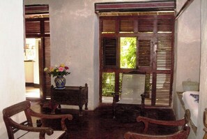 A room with a traditional wooden window, a small table with a vase of flowers, and two wooden chairs.