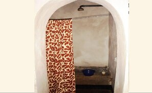 A narrow doorway with a patterned curtain, a small shelf with a bowl, and a metal fixture above.