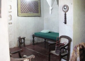 A room with a bed, a chair, a small table, and a wall-mounted decoration. - New Listing (Lamu)