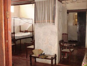 A room with a bed, a chair, a table, and a hanging mosquito net. - New Listing (Lamu)