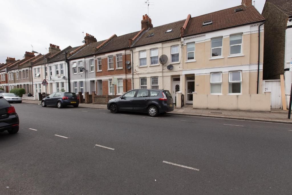A residential street with terraced houses, cars parked on the side, and a clear road.