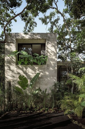 A modern building with a concrete facade, a window with curtains, and lush tropical plants surrounding it. - Casa Aviv Iconic Minimalist 4BR Design Villa (Tulum)