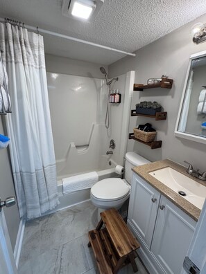 Ein Badezimmer mit Dusche, Toilette, Waschbecken und einer Holzbank.