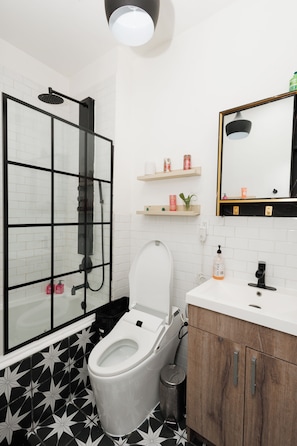 A modern bathroom with a glass shower enclosure, a white toilet, and a wooden vanity with a mirror. - Stylish Brooklyn 1-bedroom apartment with Private Backyard (Brooklyn)