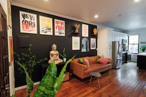 A modern living room with a brown leather sofa, a Buddha statue, and various framed pictures on the wall. - Stylish Brooklyn 1-bedroom apartment with Private Backyard (Brooklyn)