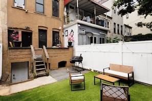 A residential backyard with a wooden staircase leading to a loft, a barbecue grill, and outdoor seating. - Stylish Brooklyn 1-bedroom apartment with Private Backyard (Brooklyn)