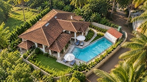 Una casa grande con piscina, rodeada de abundante vegetación.