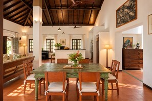 A dining area with a wooden table and chairs, a vase with flowers, and a piano in the background. - Raht Aashyana Lakhanpal Goa (Candolim)