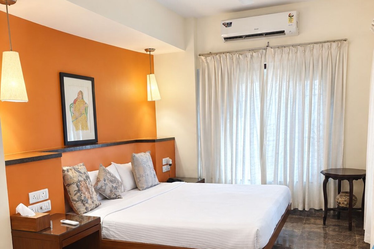 A hotel room with a bed, bedside table, nightstand, and a chair.