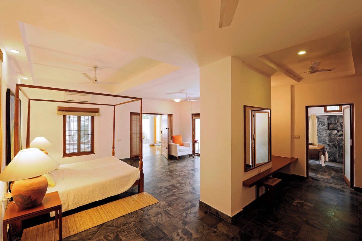 A spacious bedroom with a four-poster bed, a sitting area with a sofa, and a bathroom with a marble wall.