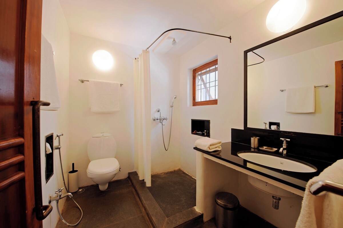 A bathroom with a toilet, shower, sink, and mirror.