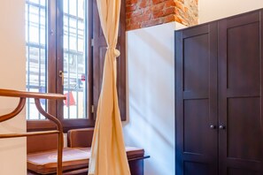 A room with a bed, a window with curtains, a door, and a bench. - Recently renovated apartment with an urban style and an authentic soul.Exposed brick walls warm the atmosphere and give real character to the space.The living area is spacious and welcoming, featuring a fully equipped kitchen, a dining table for 6 guests (Turin)