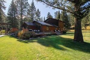 A log cabin with a porch, surrounded by a well-maintained lawn and tall trees. - The Gallatin Riverstead (Big Sky)