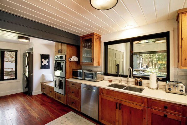 A modern kitchen with wooden cabinets, stainless steel appliances, and a large window providing a view of the outdoors. - The Gallatin Riverstead (Big Sky)