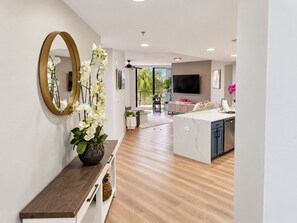 A modern kitchen with a central island, a dining area with a round table, and a living space with a TV. - Cape Harbour Marina Condo with Huge Private Veranda (Cape Coral)
