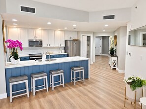 A modern kitchen with white cabinets, a central island with stools, and a microwave. - Cape Harbour Marina Condo with Huge Private Veranda (Cape Coral)