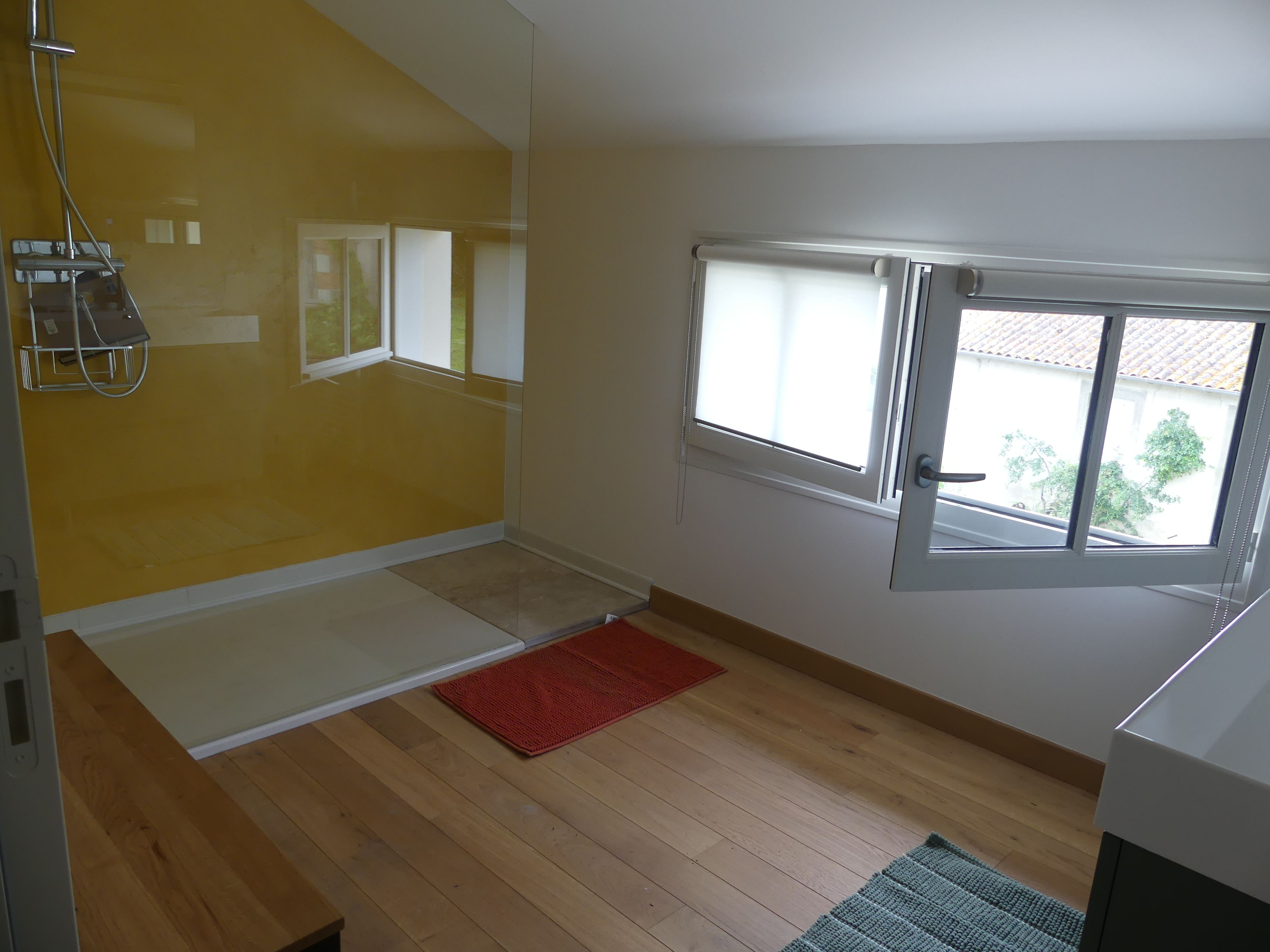 A room with a wooden floor, a red rug, a window with a view of greenery, and a white door.