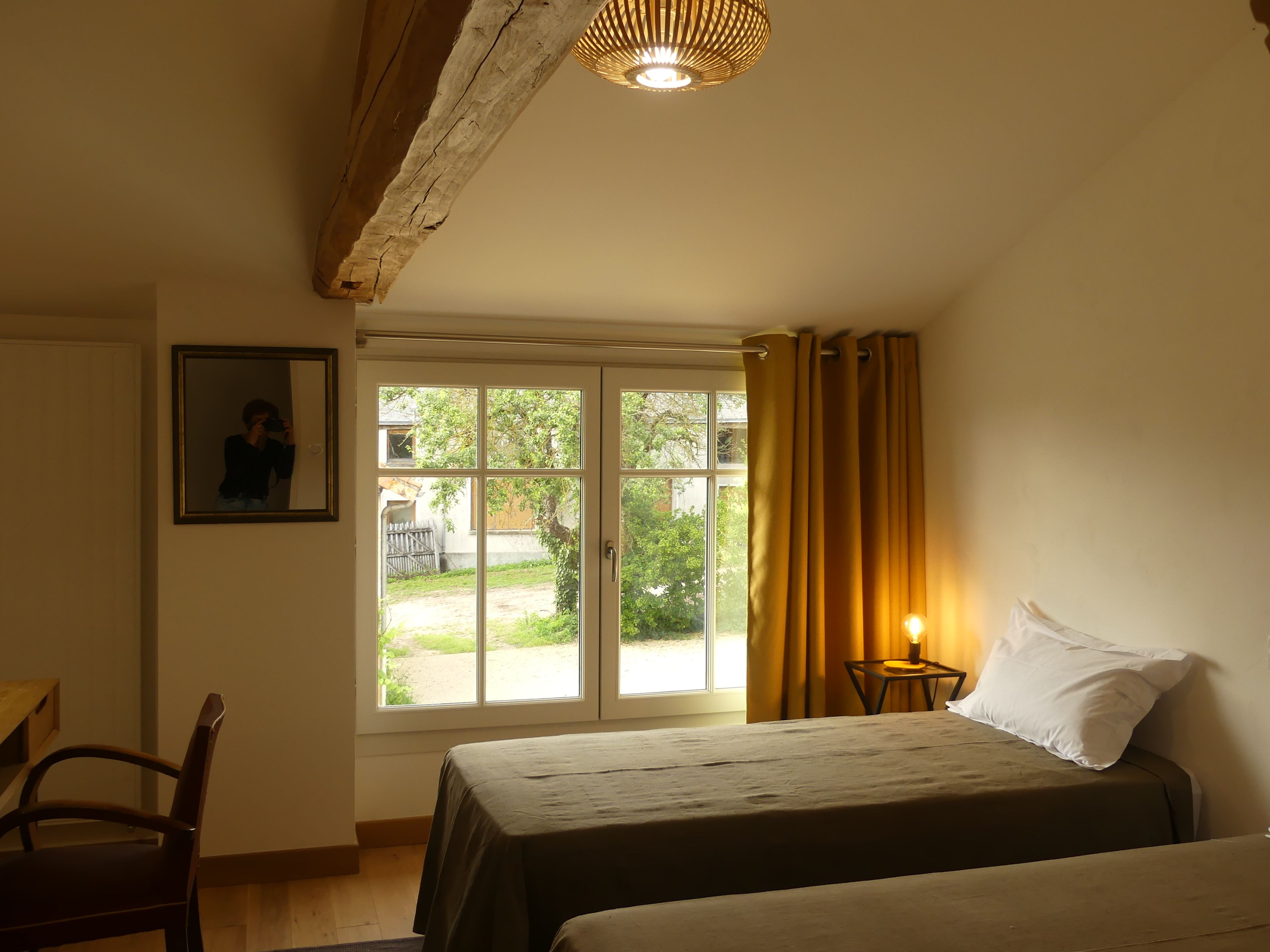 Une chambre à coucher avec un lit, une chaise, une table de chevet avec une lampe, une fenêtre avec des rideaux et un tableau encadré au mur.