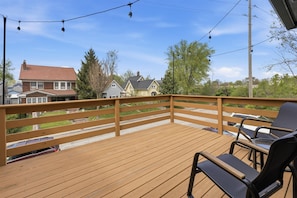 A wooden deck with a railing, outdoor seating, and a view of residential houses. - Entire 6BR Duplex near Downtown Indy, Sleeps 15 (Indianapolis)