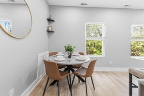 A dining area with a round table set for four, surrounded by chairs, with a plant centerpiece and a vase on a shelf. - Entire 6BR Duplex near Downtown Indy, Sleeps 15 (Indianapolis)