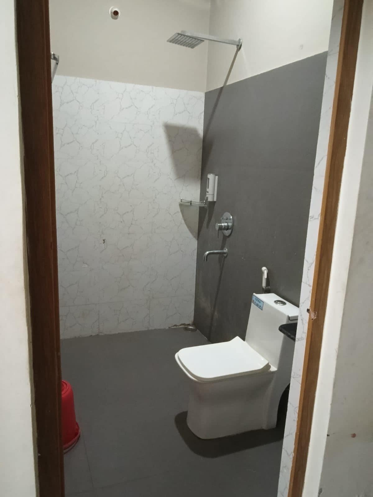 A bathroom with a toilet, a shower, and a red trash bin.