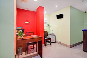 A room with a red wall, a desk with a chair, a small table with a plant, and a water dispenser. - Hotel O Tower Shanavi Inn (Barasat)