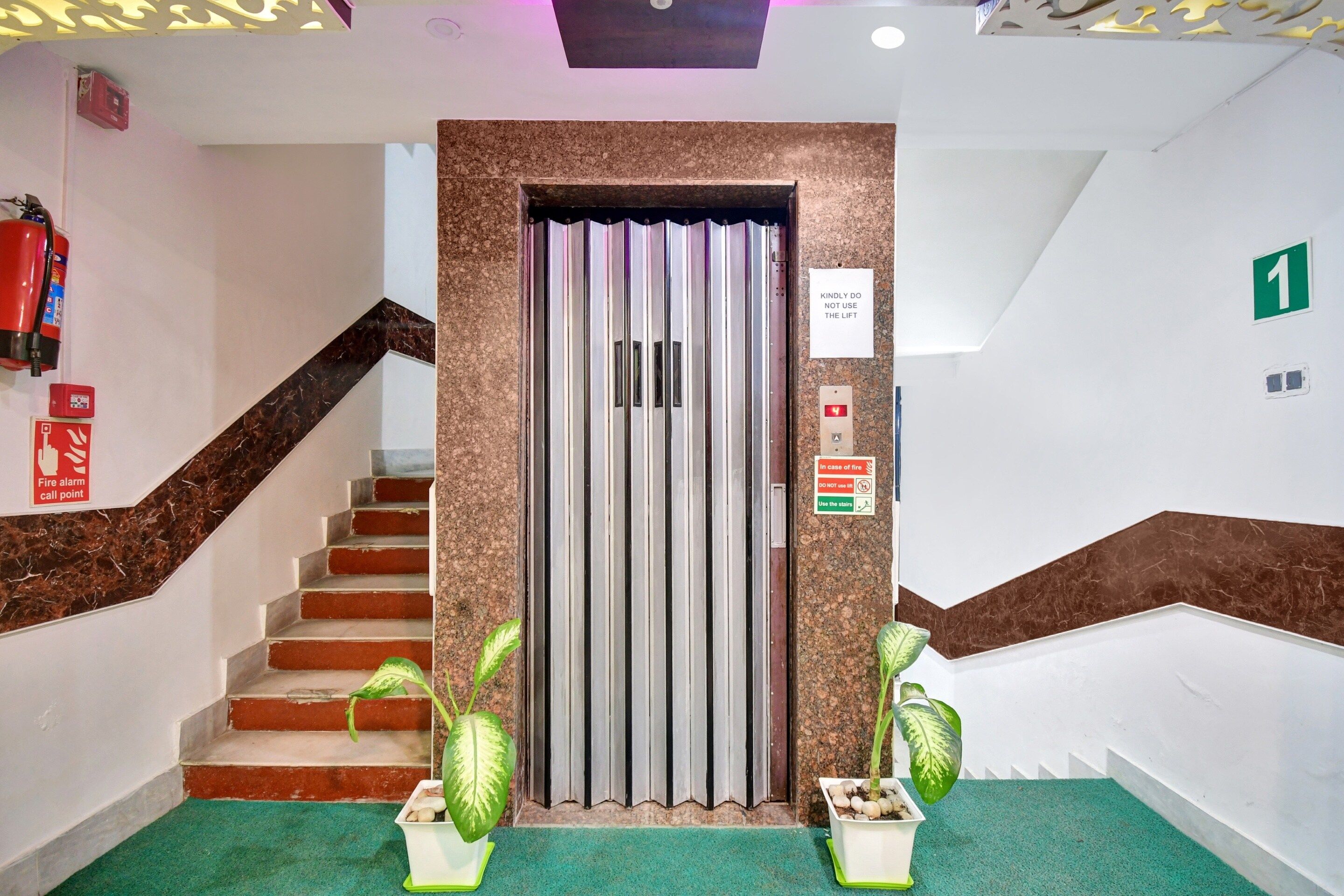 Entrada de un hotel con escaleras, ascensor y señalización de emergencia.