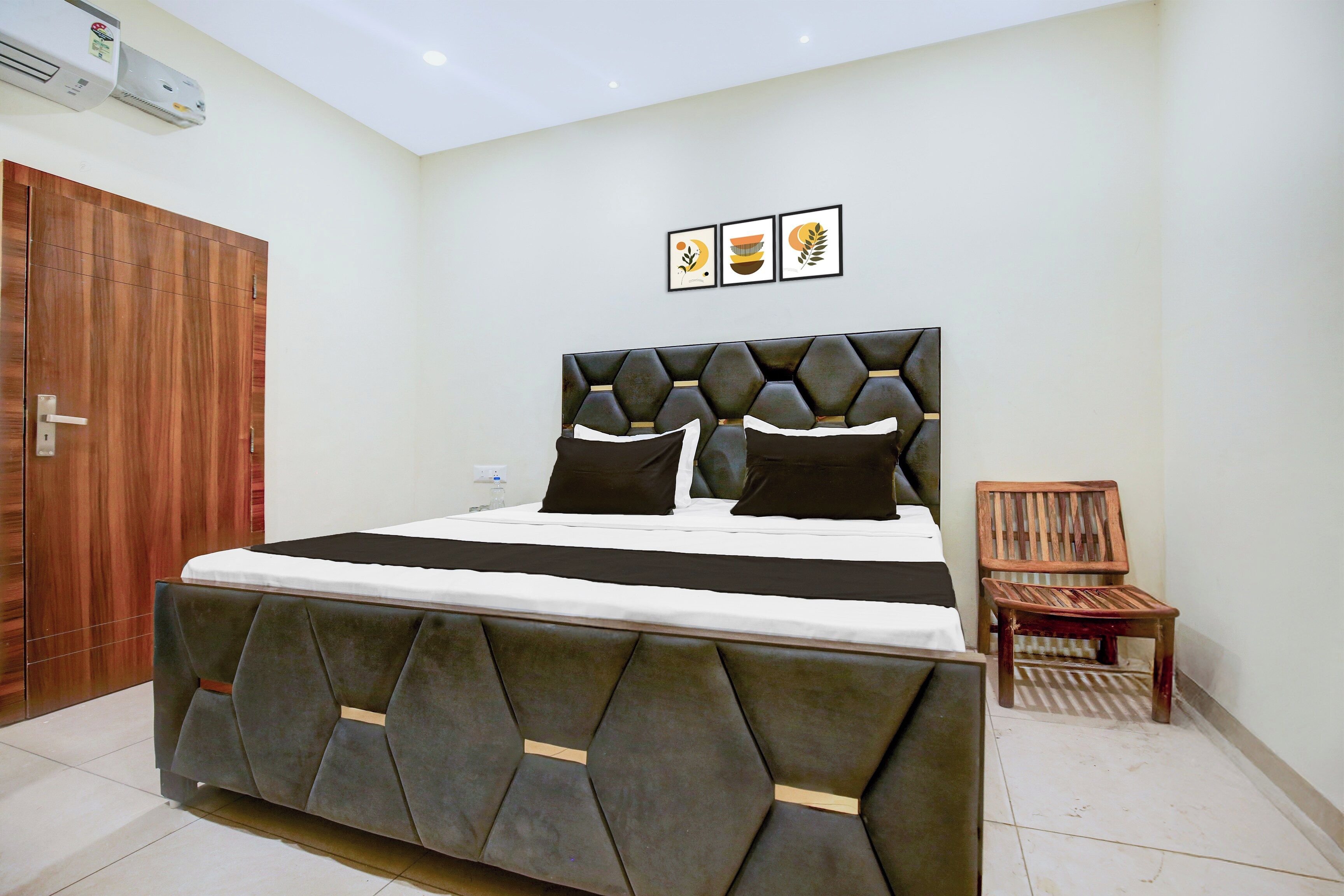 Une chambre à coucher avec un lit, une porte en bois, une petite chaise en bois et un climatiseur fixé au mur.