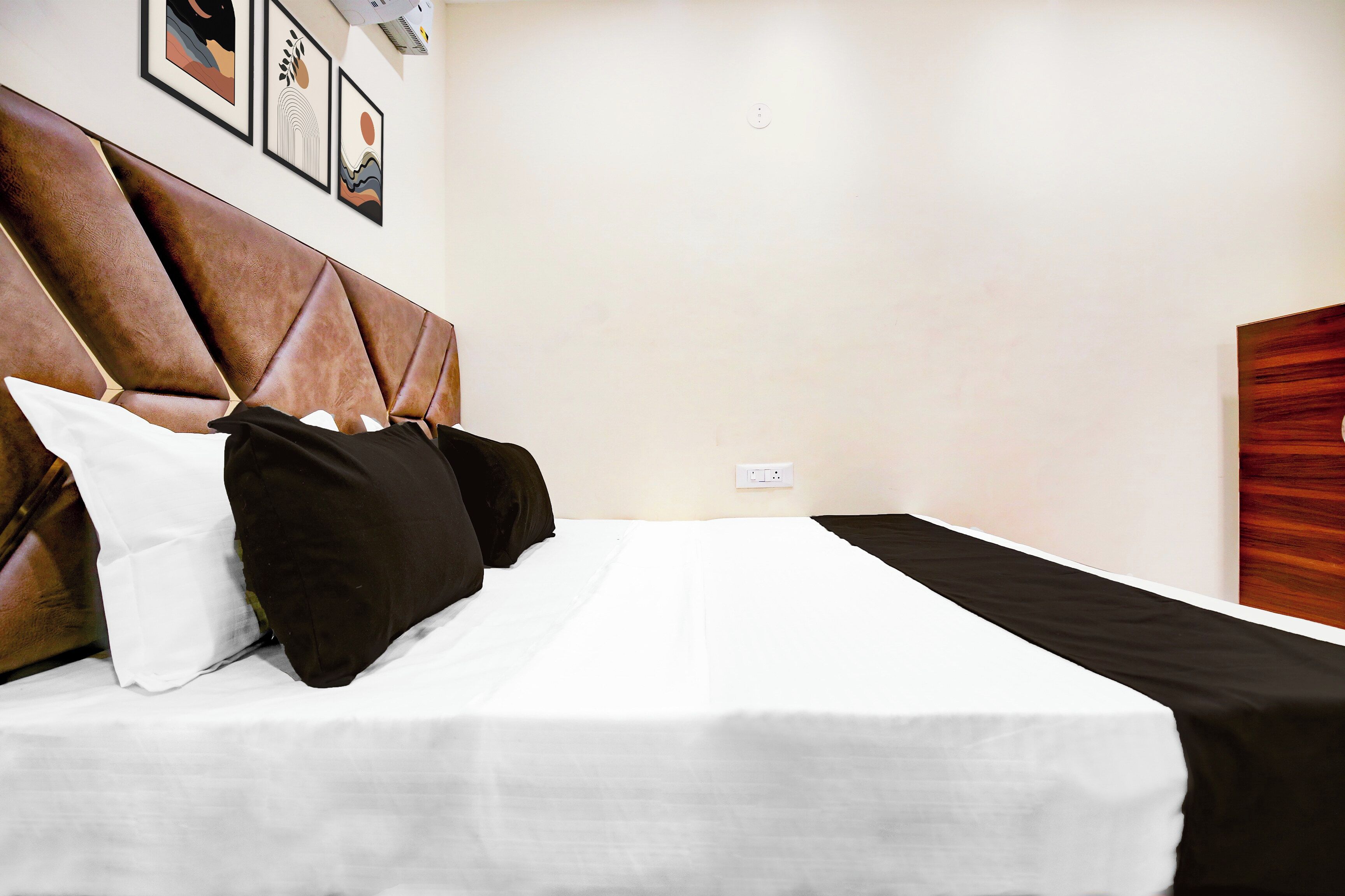 A hotel room with a bed, pillows, a headboard, and a wall with framed pictures.