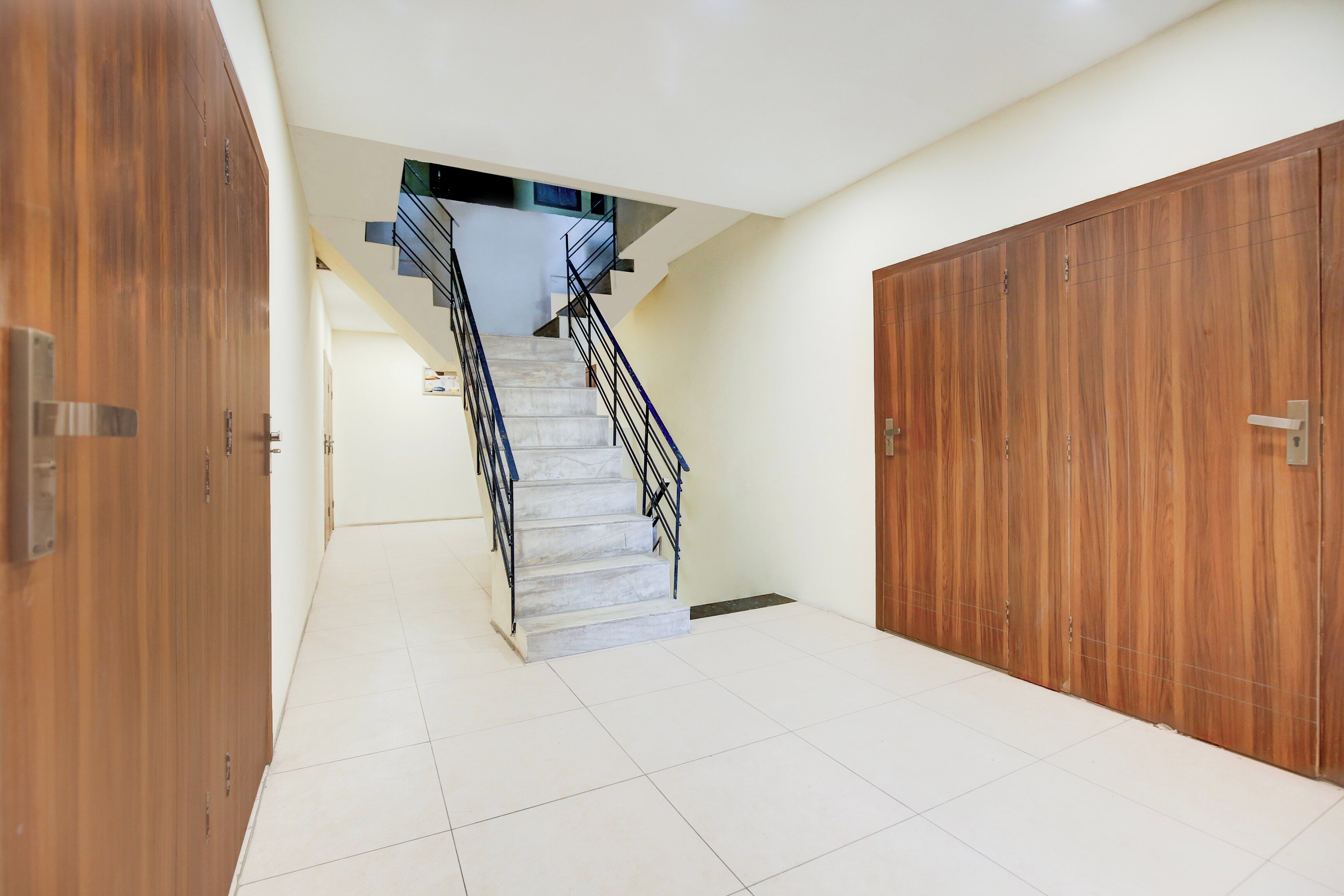 Un couloir avec un escalier menant à un palier, bordé de placards en bois et doté d’un sol carrelé.