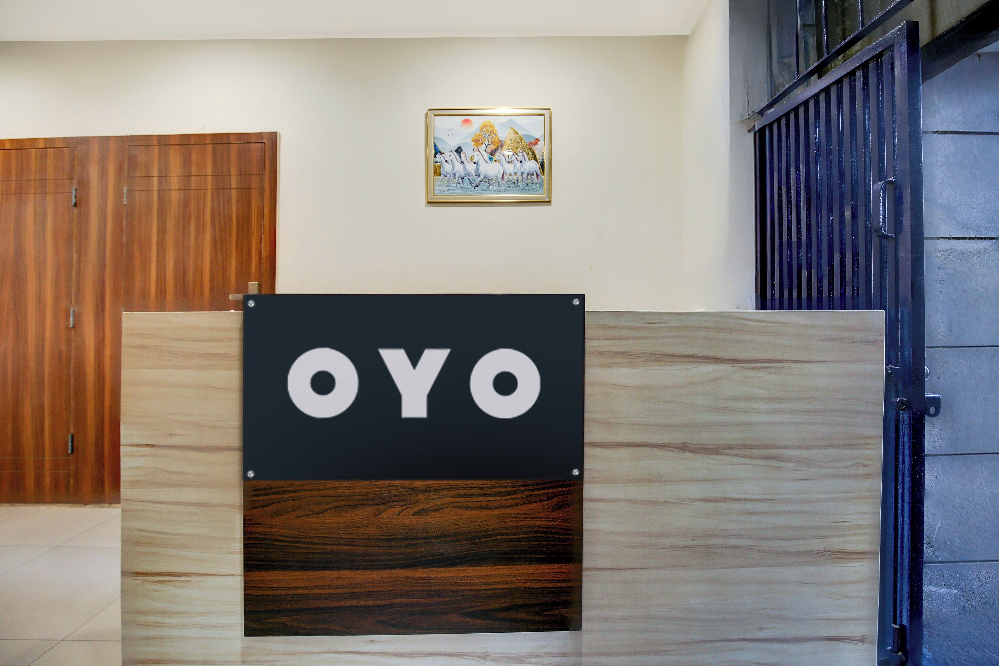 A sign with the word 'OYO' on a wooden panel, a wooden door, a framed picture on the wall, and a metal gate.