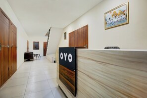 A hotel reception area with a wooden reception desk, a sign that reads 'OYO', and a framed picture on the wall.