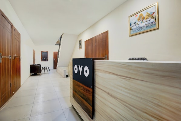 Un espace d’accueil d’hôtel avec un comptoir de réception en bois, une enseigne indiquant « OYO » et un tableau encadré accroché au mur.