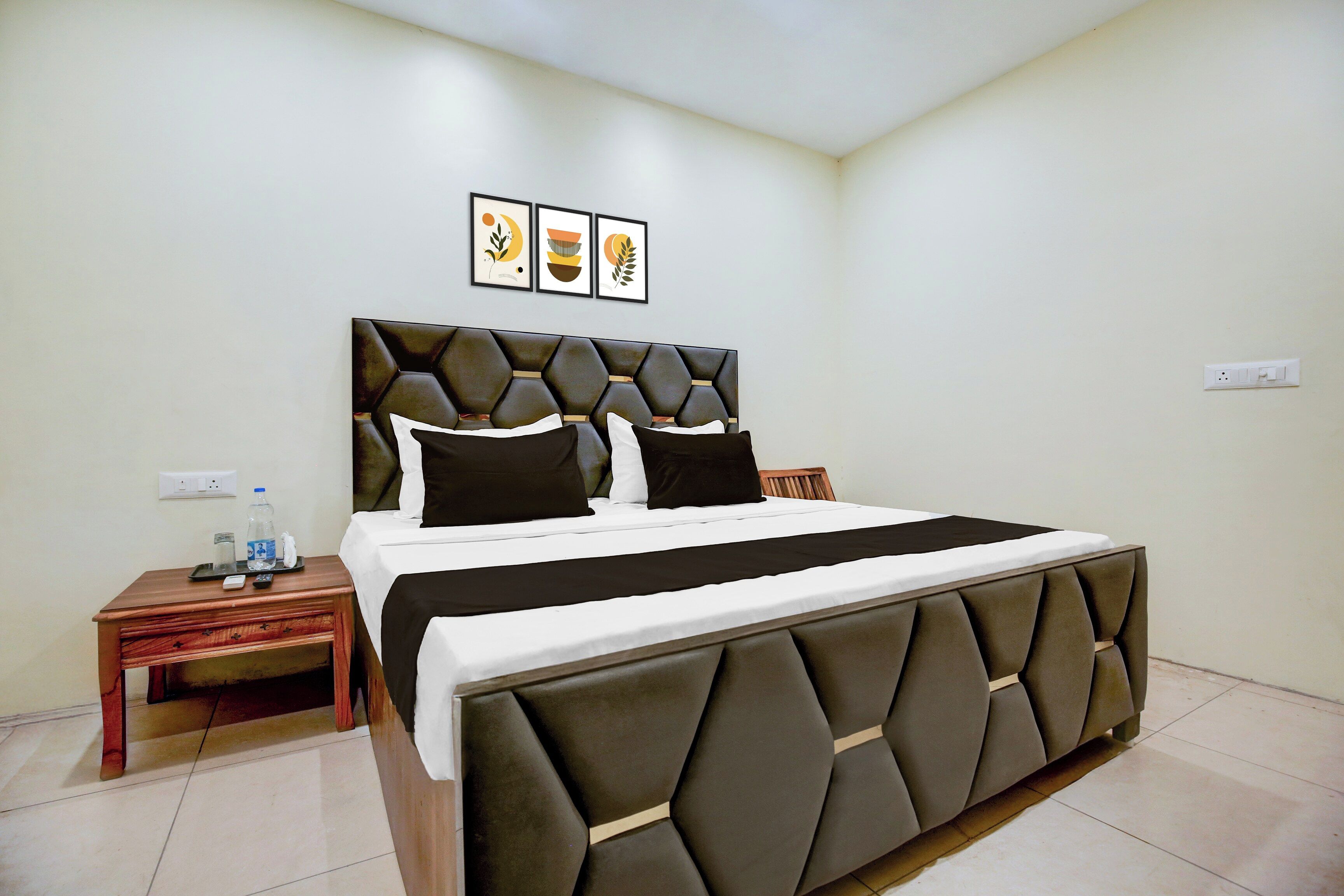 A hotel room with a large bed, a wooden nightstand, a water bottle, and a framed picture on the wall.