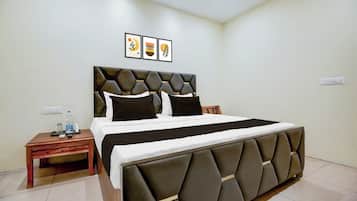 A hotel room with a large bed, a wooden nightstand, a water bottle, and a framed picture on the wall.