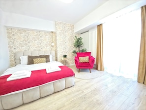 A hotel room with a large bed, a red armchair, a small side table, and a potted plant. - Spacious Luxurious Central 4-bedroom apartment in Bucuresti next to Old Town (București)