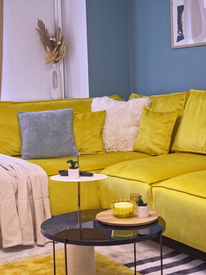 A yellow sofa with a white fluffy throw, a grey pillow, and a small table with a plant and a candle. - Spacious Luxurious Central 4-bedroom apartment in Bucuresti next to Old Town (București)