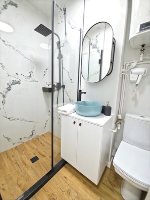 Casa de banho moderna com cabine de duche em vidro, lavatório branco com cuba azul, espelho e sanita.