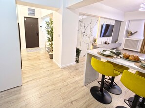 A modern kitchen with a marble backsplash, a flat-screen TV, and a dining area with yellow chairs. - Spacious Luxurious Central 4-bedroom apartment in Bucuresti next to Old Town (București)