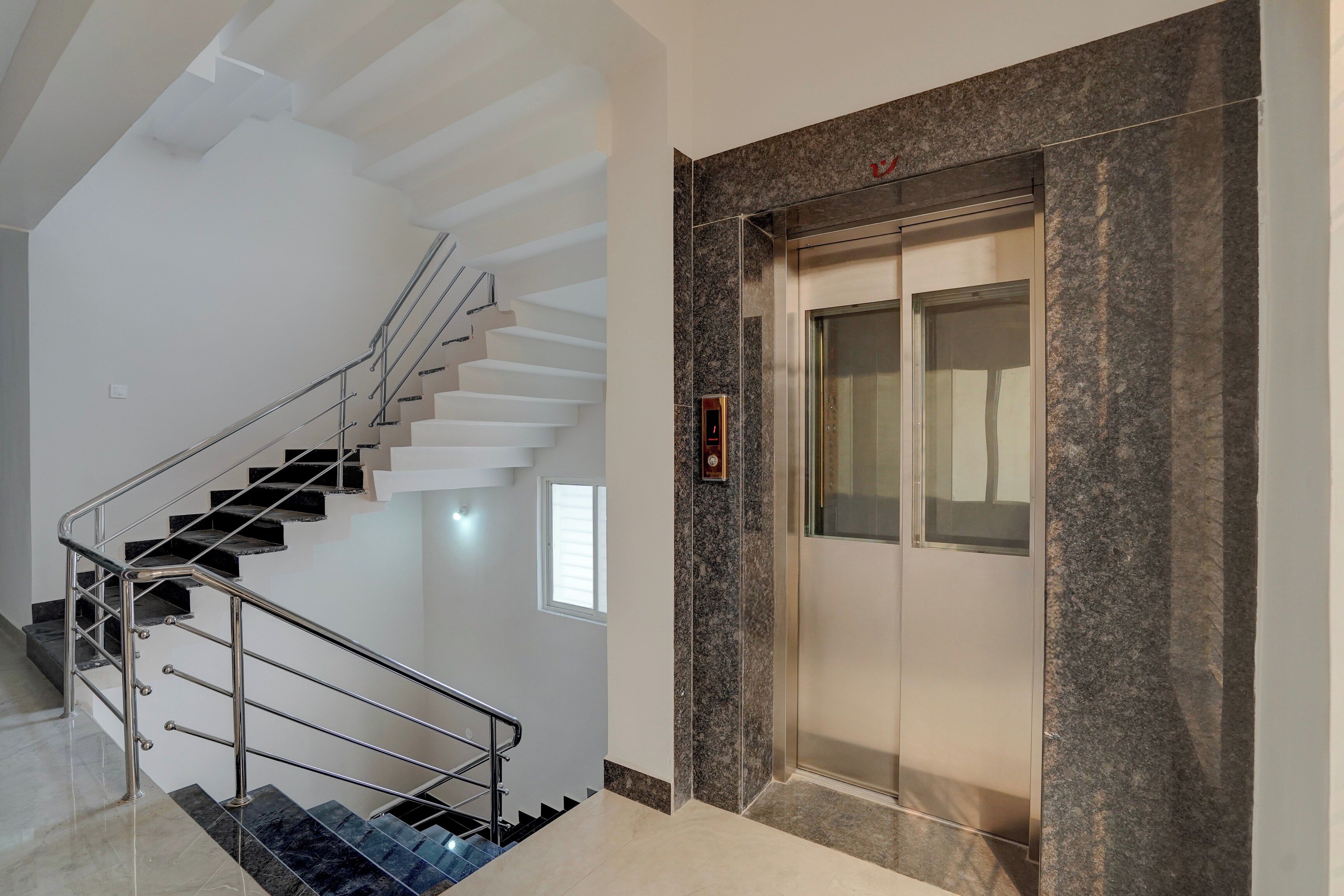 Un ascensor moderno con detalles de mármol, una escalera con barandillas metálicas y un pequeño ventanal.