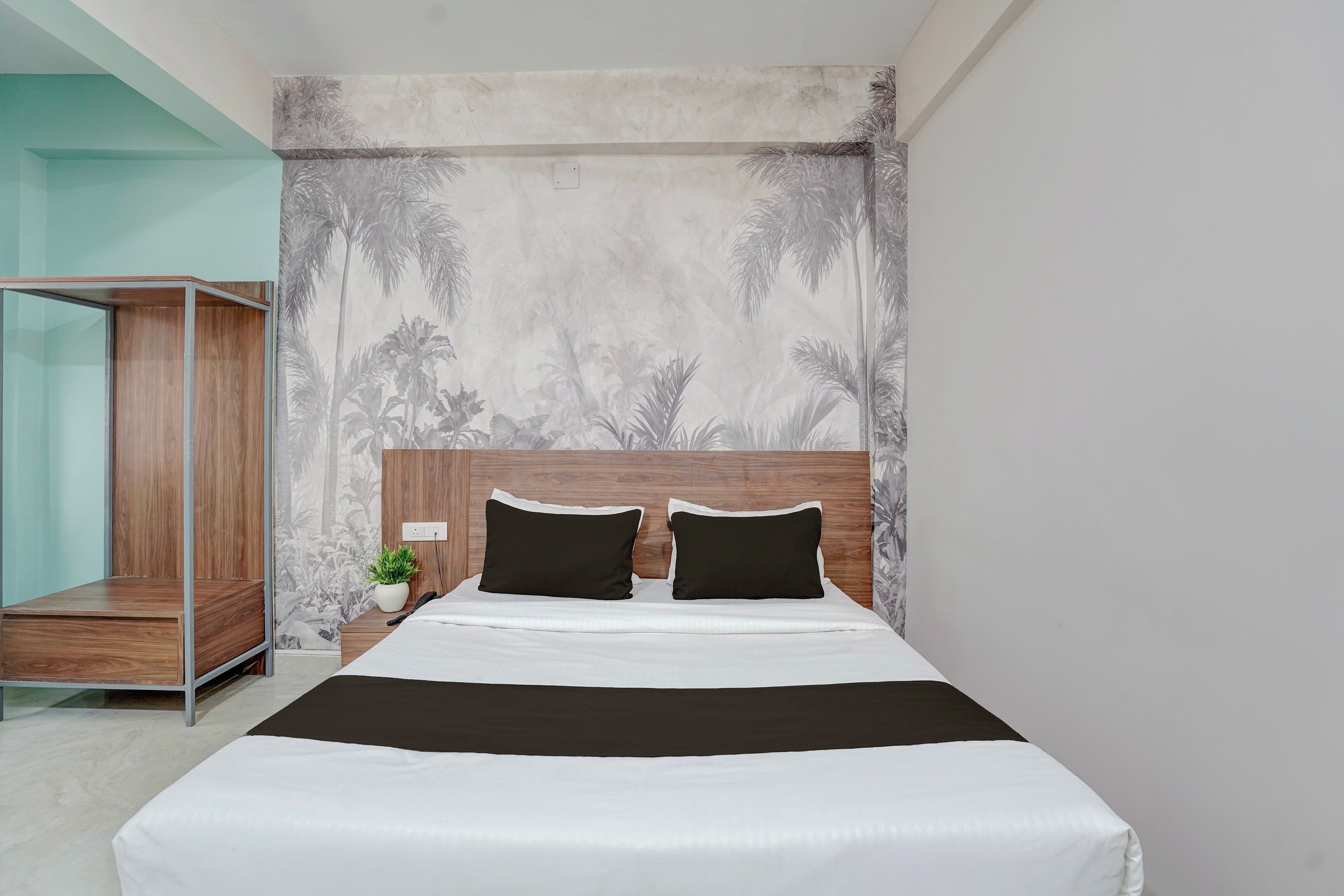 A modern bedroom with a large bed, a wooden headboard, and a wall mural of tropical foliage.