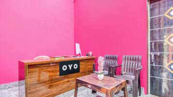 A reception desk with a sign reading 'OYO' in a room with pink walls and a wooden door.