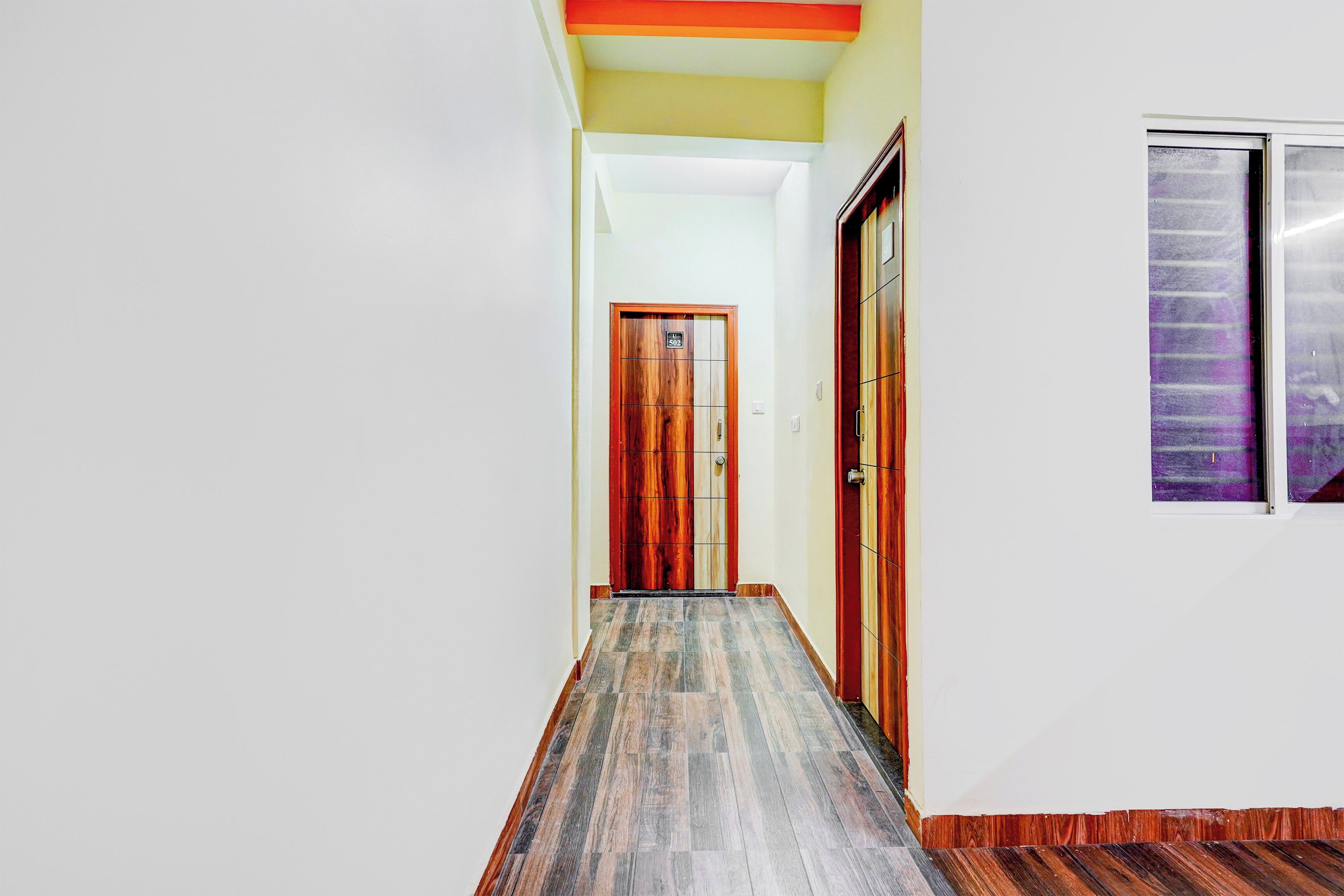 Un pasillo con una puerta de madera, un ventanal con vistas moradas y un suelo de baldosas.
